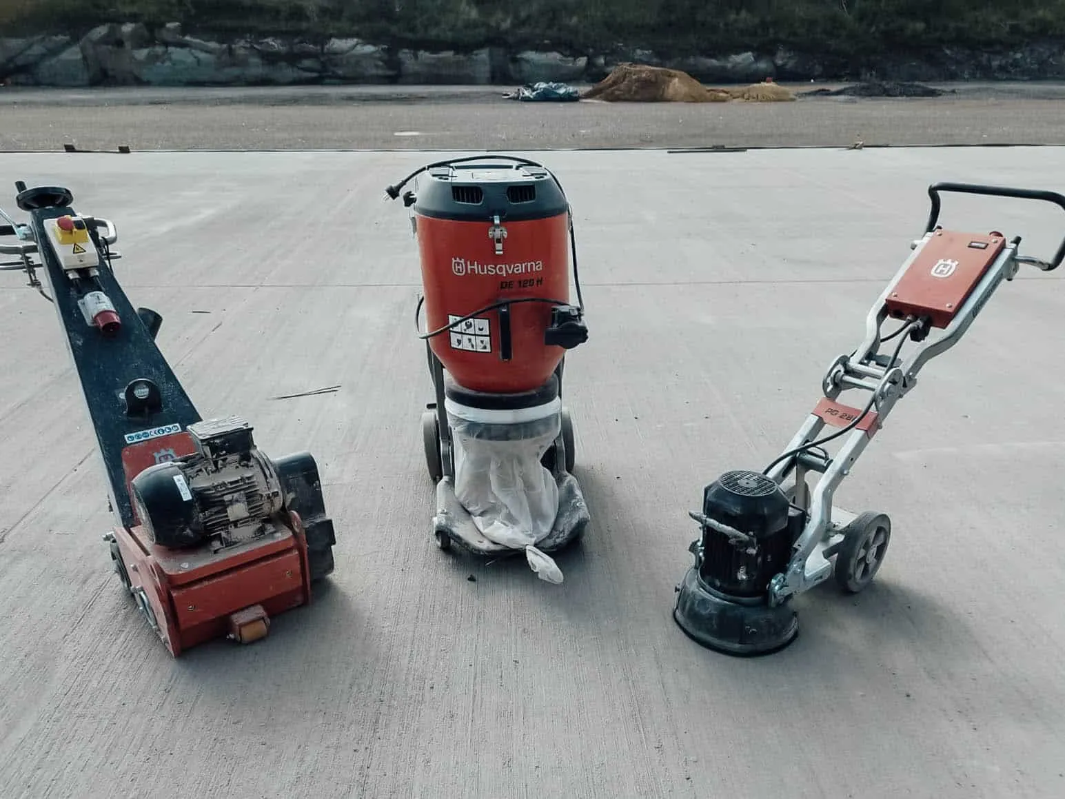 Zwei Bodenschleifmaschinen und ein Industriesauger auf einer großen Betonfläche im Freien