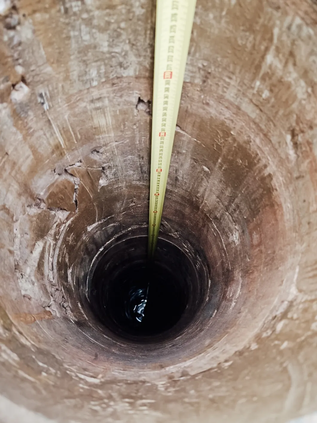 Blick in eine tiefe, frisch gesetzte Kernbohrung in einer Betondecke, daneben ein Zollstock zur Durchmesserkontrolle