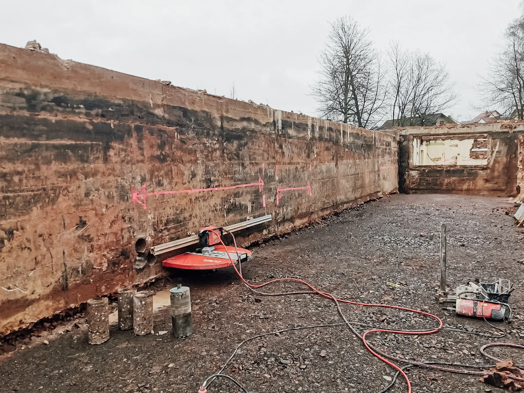 Lange Baugrube mit gesägter Betonwand, roter Wandsäge auf der Schiene und ausgelegten Bohrkernen